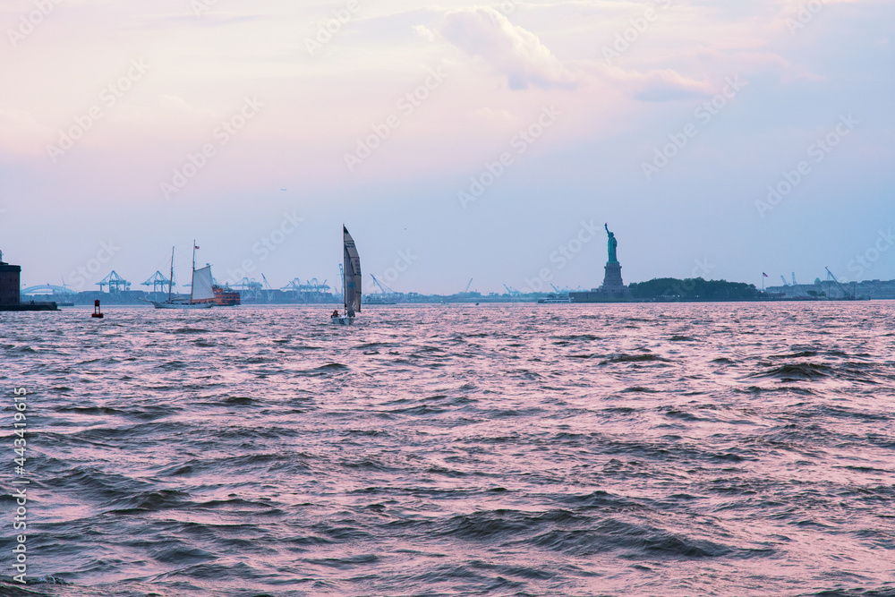 Sailboats and the Statue of Liberty at sunset in New York Harbor.