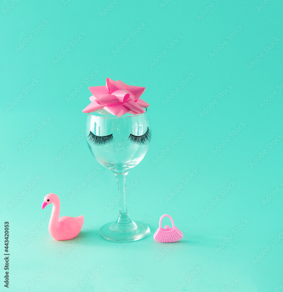 Glass cup with eyelashes, pink bow and women's accessories. Turquoise background. Minimalism. Glass cup with eyelashes, pink bow and women's accessories. Turquoise background. Minimalism.