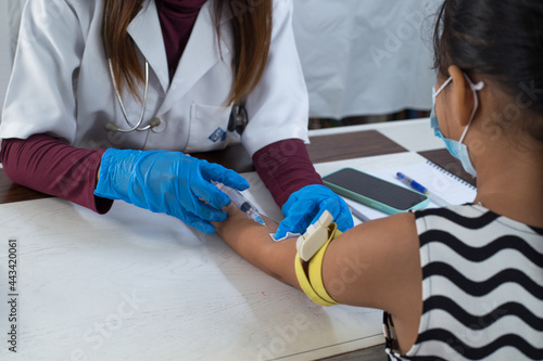 doctor taking blood sample from a young child with syringe, wearing protective gloves. 