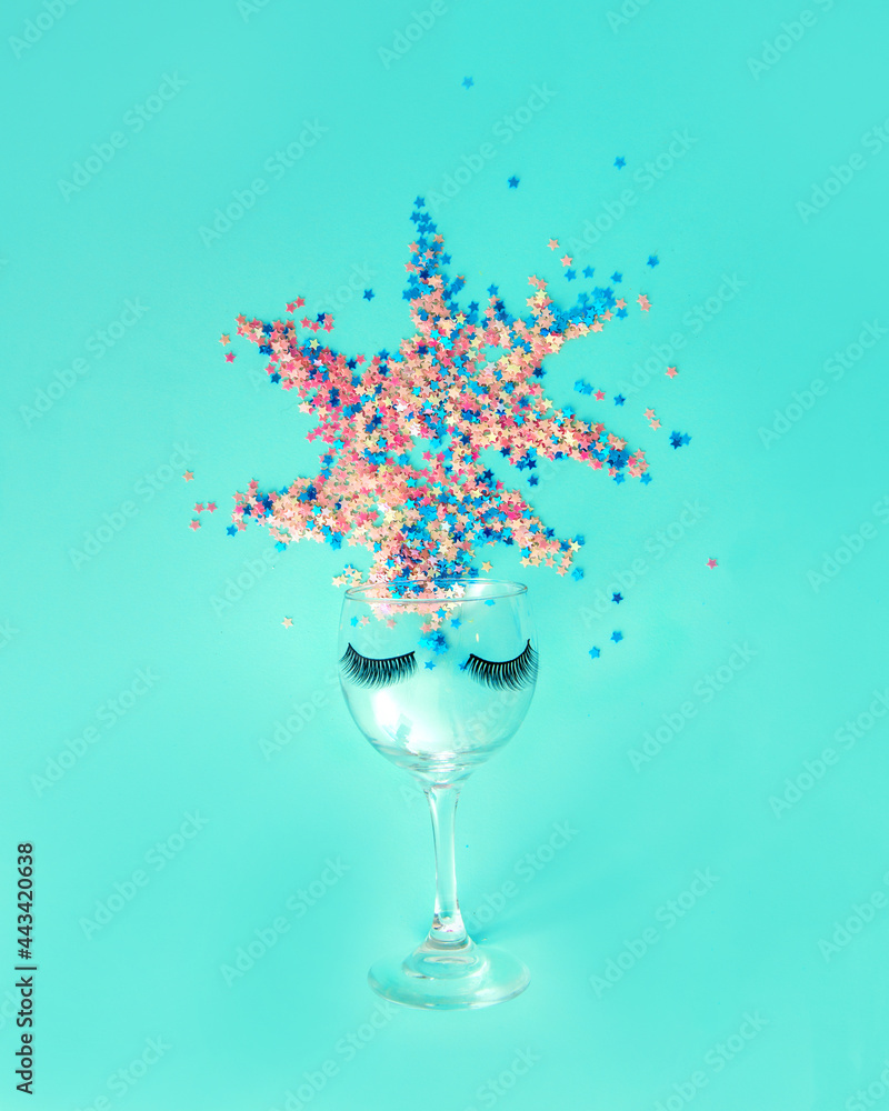 A glass with eyelashes from which he exposes sequins in height. A party, a women's celebration. Minimal composition.