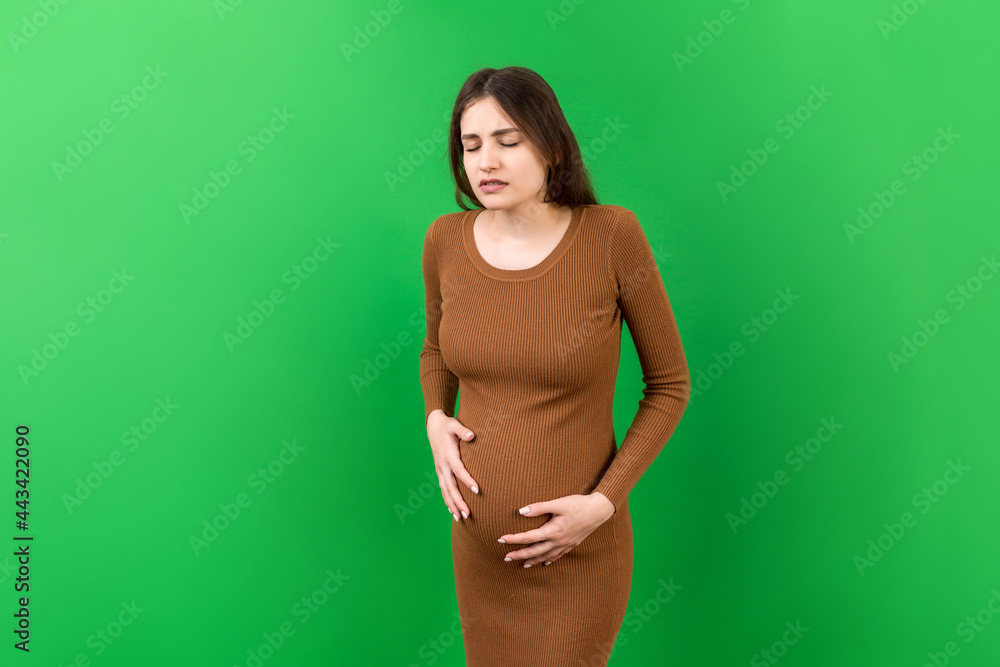 a pregnant girl who has a stomach ache stands on a colored background. isolated a pregnant girl who has a stomach ache stands on a colored background. isolated