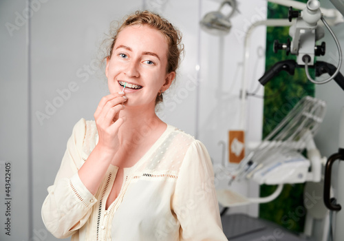 Portrait of a beautiful woman in well equipped dentist s office demonstrating interdental brushing. Young girl wears dental ceramic and metal braces. Concept of dentistry  hygiene and oral care.