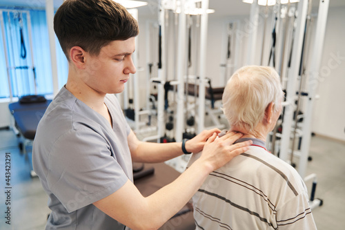 Young physical therapist pressing on pensioner neck with two fingers