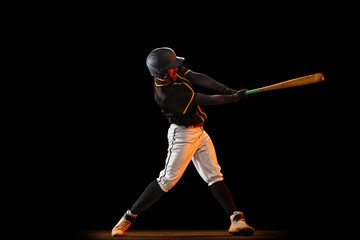 Professional baseball player, pitcher in sports uniform and equipment playing baseball isolated on black studio background in neon light. Team sport concept
