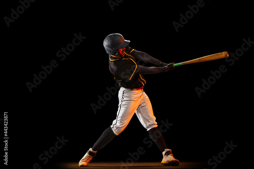 Professional baseball player, pitcher in sports uniform and equipment playing baseball isolated on black studio background in neon light. Team sport concept