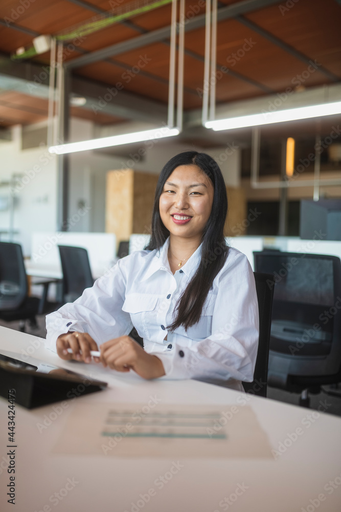 Smiling Asian woman working in office and looking at camera Smiling Asian woman working in office and looking at camera