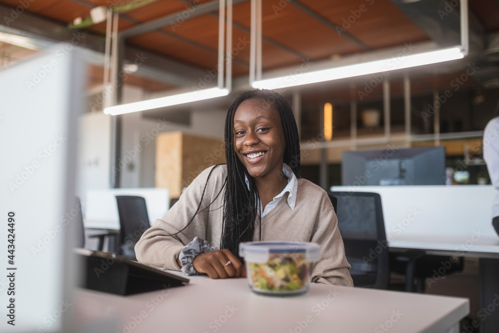 Content black woman sitting at table in office during lunch Content black woman sitting at table in office during lunch
