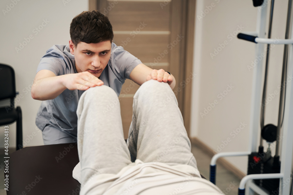 Determined therapist lowering legs of person on medical couch