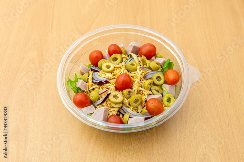 Pulled chicken salad with sliced green olives, diced ham, cherry tomatoes, iceberg lettuce and red onion in a home delivery container