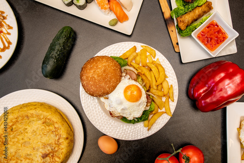 Hamburger with fried egg, potato omelette, cucumber and peppers on gray table