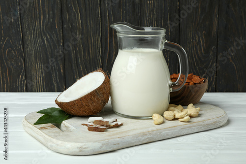 Pitcher of milk, coconut and nuts on white wooden table
