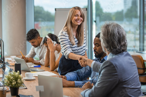 Two business people shaking hands while sitting in meeting room. Businesswoman shake hands to businessman. Portrait of happy smiling woman signing off deal with an handshake.