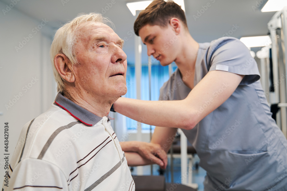 Aged male sitting on couch and being tended by physician Aged male sitting on couch and being tended by physician