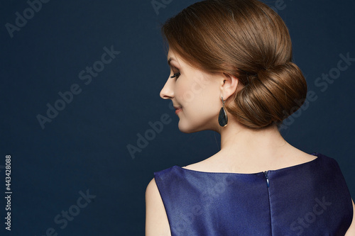 Young woman with bright makeup and elegant hairdo wearing blue dress posing on the blue background. A portrait of an elegant model with evening coiffure over blue background