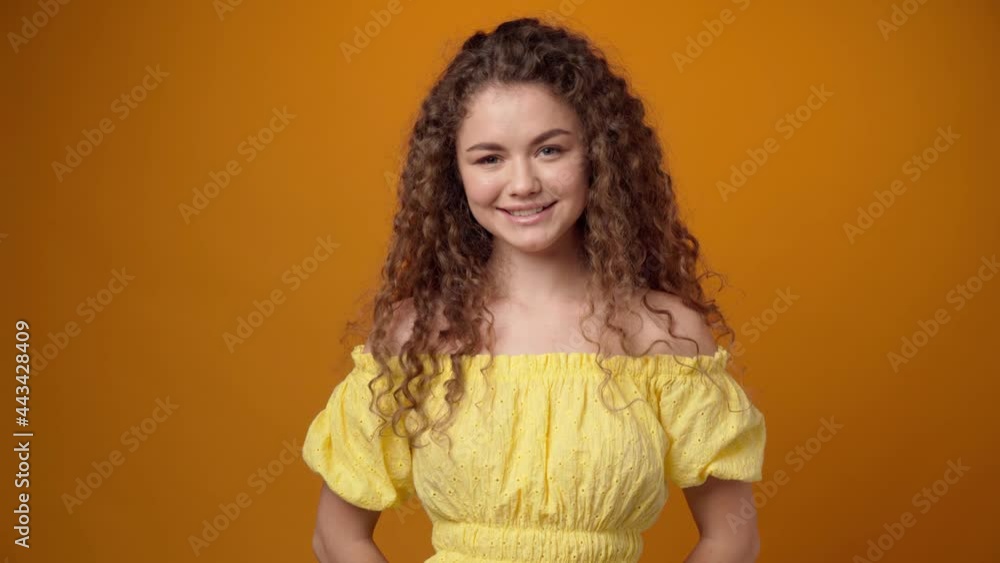 Young curly haired woman showing thumbs up sign against yellow background Young curly haired woman showing thumbs up sign against yellow background