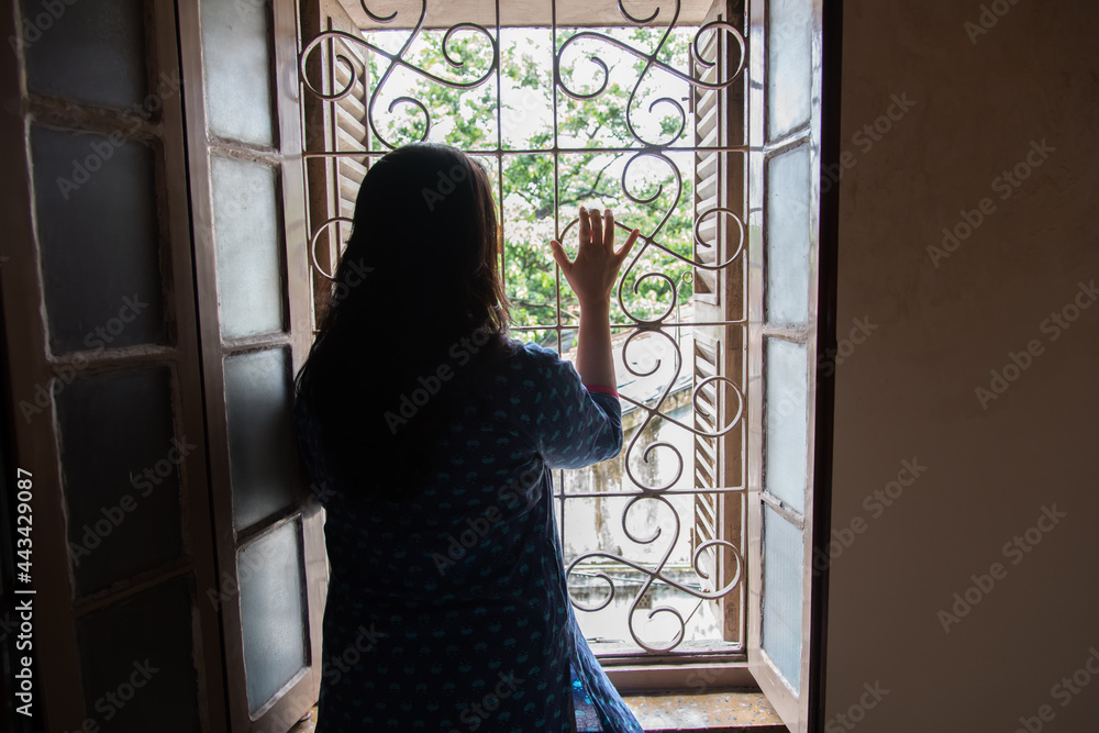 Backside view of a woman on the window front. Concept of quarantine, confinement. Backside view of a woman on the window front. Concept of quarantine, confinement.