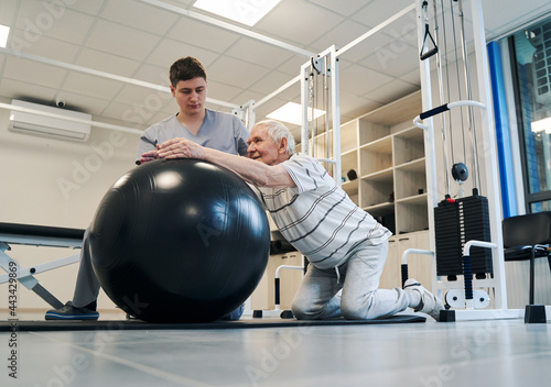 Pensioner standing on knees while putting arms on exercise ball