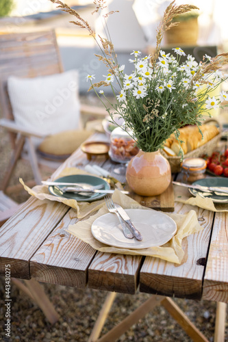 Beautifully served wooden table in natural boho style outdoors. Dining table decorated with field flowers, dishes and fresh food