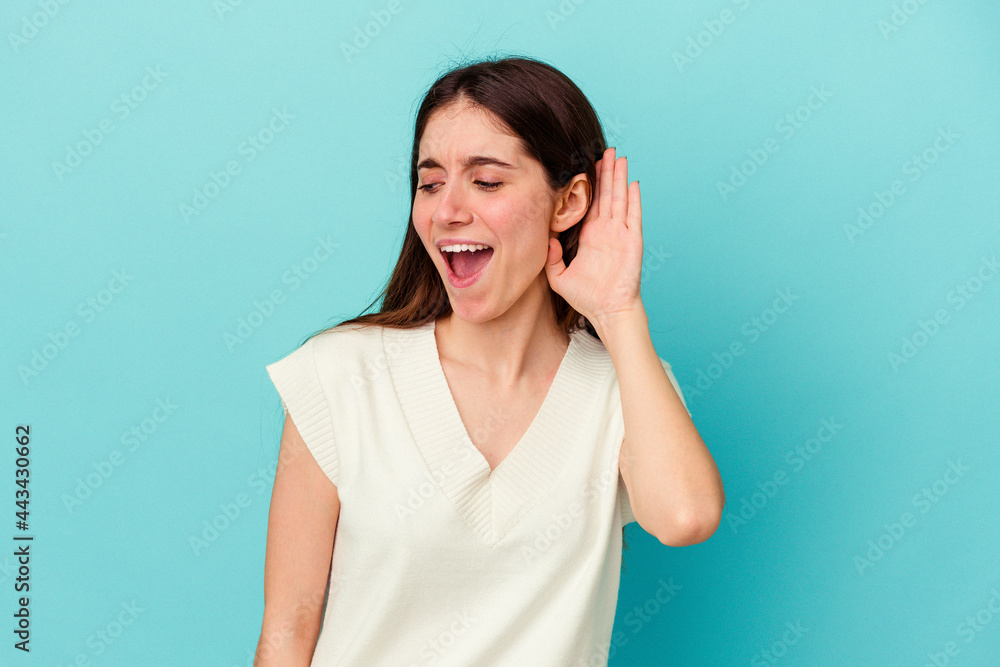 Young caucasian woman isolated on blue background trying to listening a gossip. Young caucasian woman isolated on blue background trying to listening a gossip.