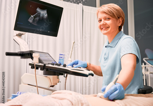 Woman sonographer examining patient with ultrasound scanner. Doctor smiling while performing ultrasound scanning in gynecological cabinet. Concept of health, sonography and ultrasound diagnostics. photo