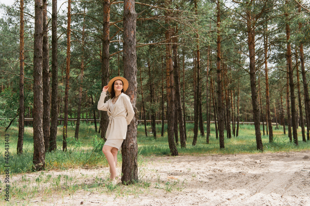 full length of cheerful young woman adjusting straw hat and standing in woods full length of cheerful young woman adjusting straw hat and standing in woods