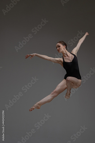 Professional leaping ballerina dancing against gray background