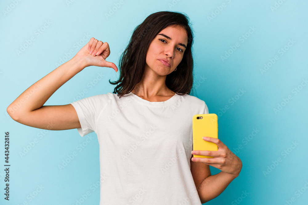 Young caucasian woman holding a mobile phone isolated on blue background feels proud and self confident, example to follow. Young caucasian woman holding a mobile phone isolated on blue background feels proud and self confident, example to follow.
