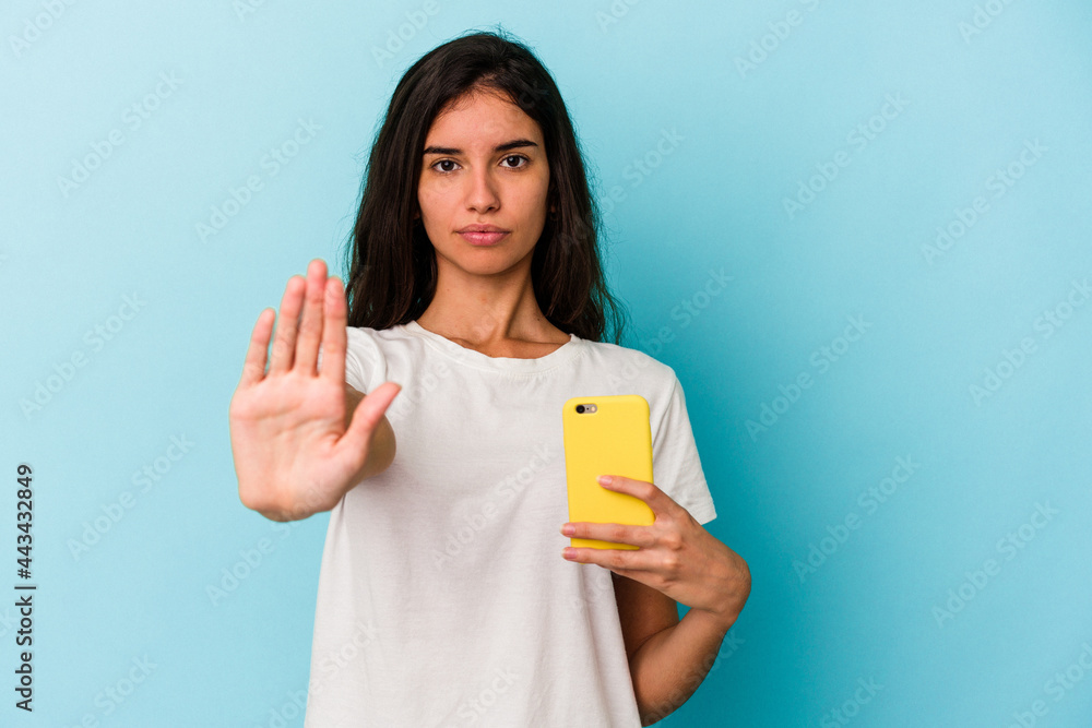 Young caucasian woman holding a mobile phone isolated on blue background standing with outstretched hand showing stop sign, preventing you. Young caucasian woman holding a mobile phone isolated on blue background standing with outstretched hand showing stop sign, preventing you.