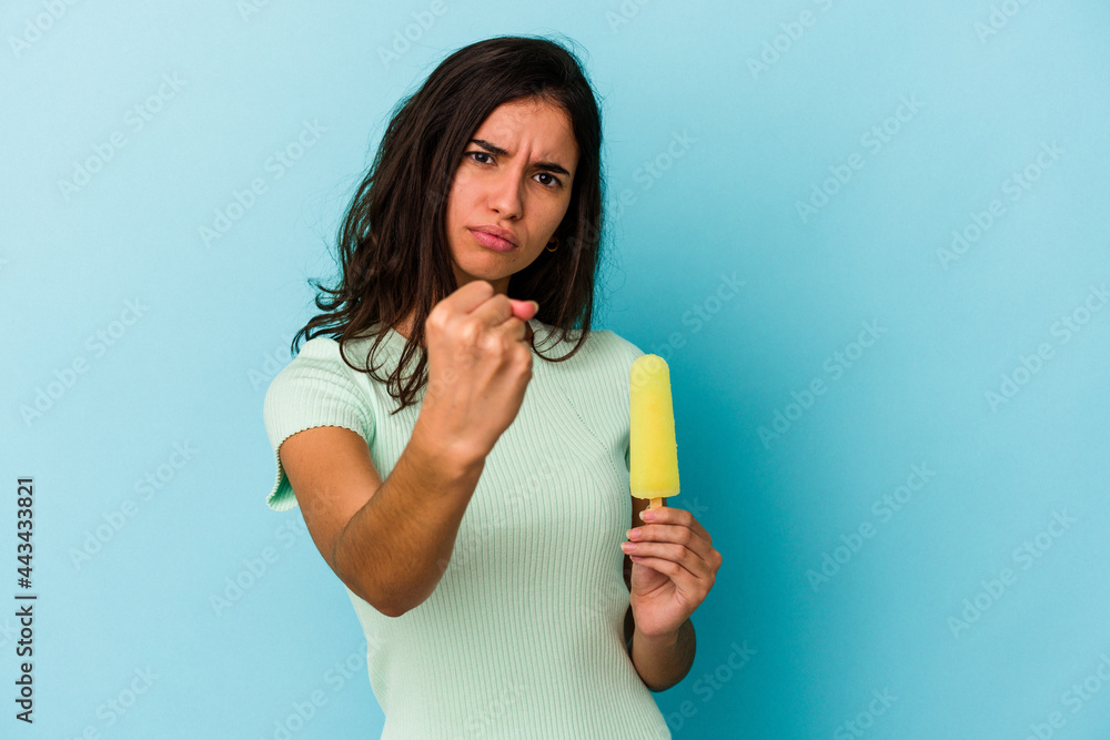 Young caucasian woman holding an ice cream isolated on blue background showing fist to camera, aggressive facial expression. Young caucasian woman holding an ice cream isolated on blue background showing fist to camera, aggressive facial expression.