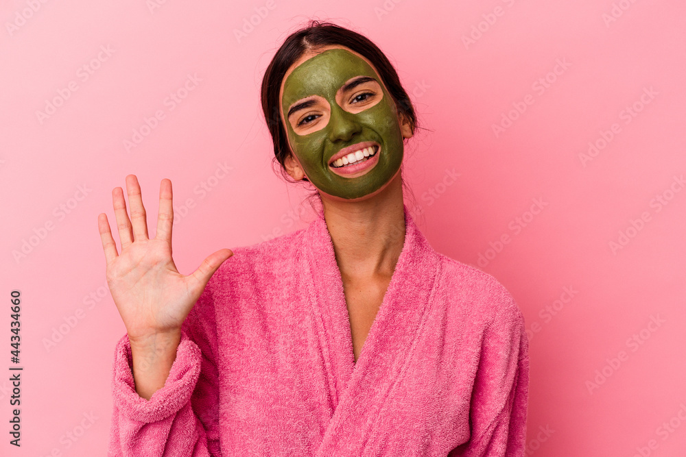 Young caucasian woman wearing a bathrobe and facial mask isolated on pink background smiling cheerful showing number five with fingers. Young caucasian woman wearing a bathrobe and facial mask isolated on pink background smiling cheerful showing number five with fingers.