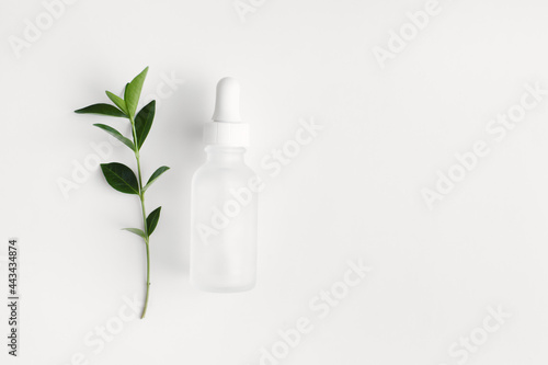 Cosmetic glass bottle with pipette, green leaves on white background. Skincare beauty product. Flat lay, top view, copy space