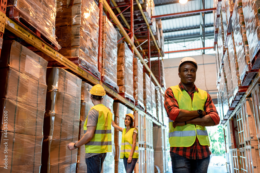 Portrait of black male worker team working in factory warehouse. Black man worker smiling with crossed arms indoor of building in background shelves with goods.Logistic industry concept. Portrait of black male worker team working in factory warehouse. Black man worker smiling with crossed arms indoor of building in background shelves with goods.Logistic industry concept.