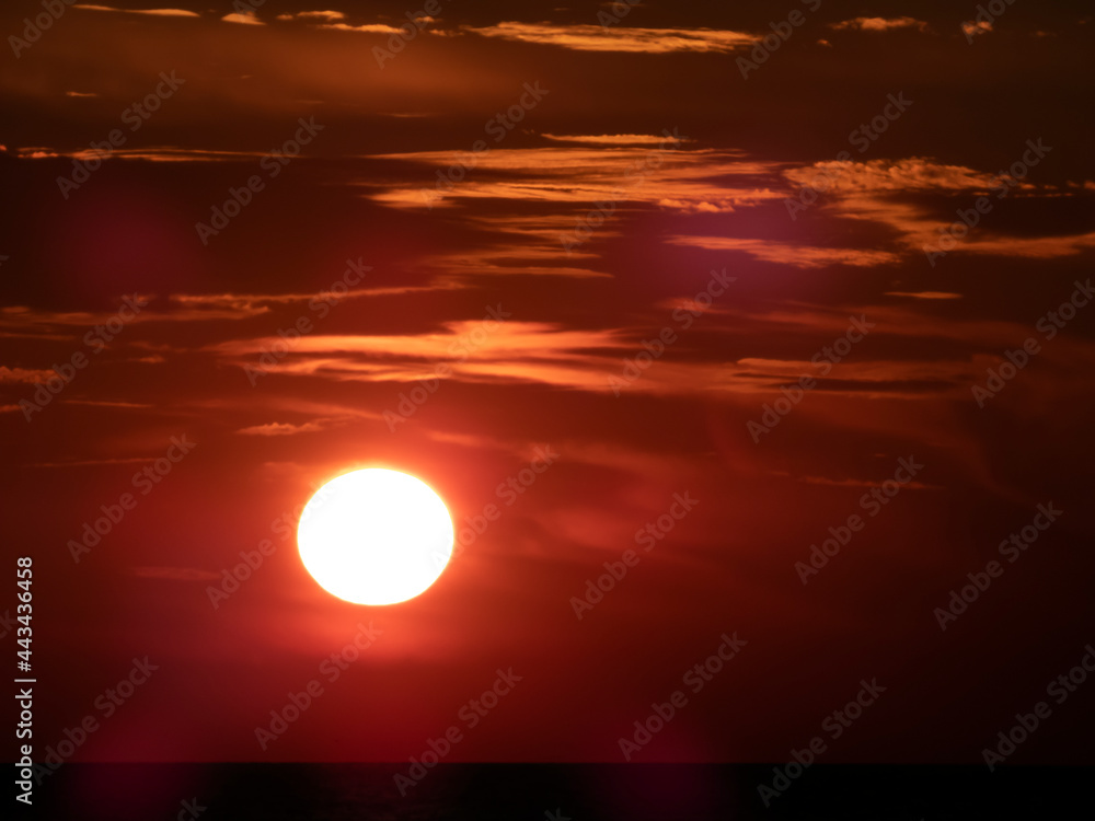 Red sunset on the sea coast, the sun on a dark background of sky and clouds
