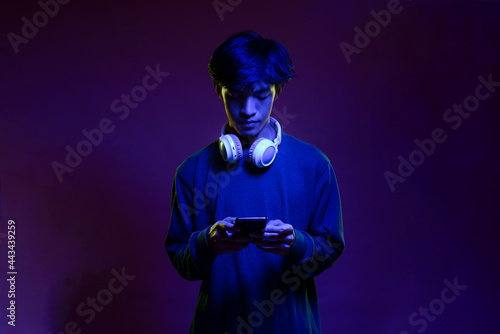 Portrait of handsome young asian man holding then looking at the mobile phone wearing headphone in neon light