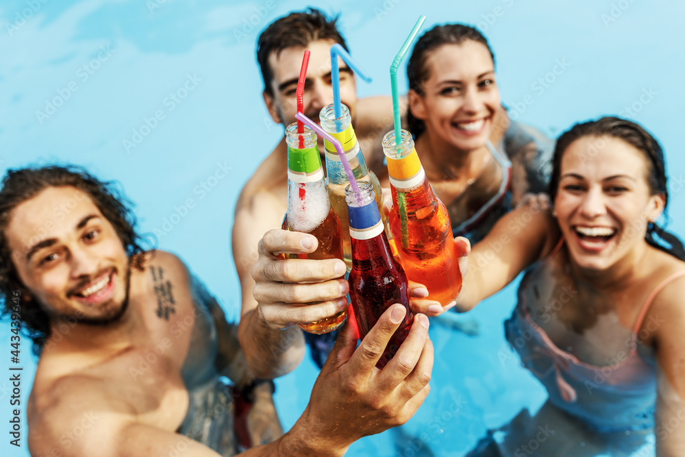 A group of young people refreshing in the swimming pool and toasting together with cold drinks. A group of young people refreshing in the swimming pool and toasting together with cold drinks.