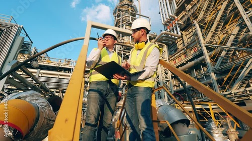 Outdoor premises of the oil refinery with two engineers talking