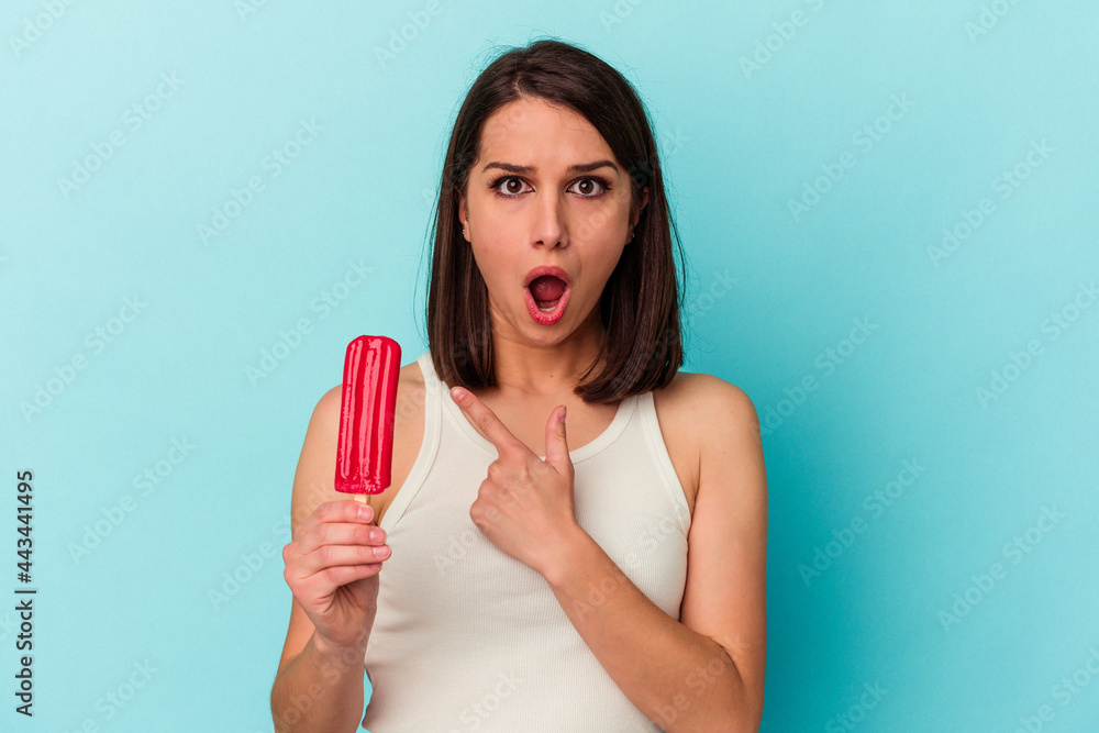 Young caucasian woman holding an ice cream isolated on blue background pointing to the side Young caucasian woman holding an ice cream isolated on blue background pointing to the side