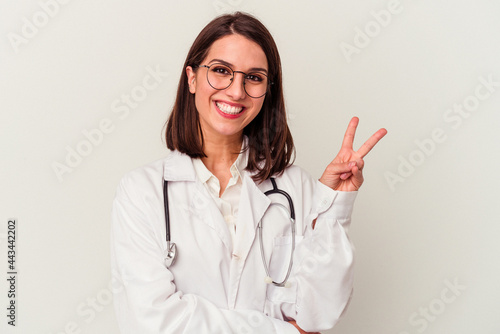 Young doctor caucasian woman isolated on white background joyful and carefree showing a peace symbol with fingers.