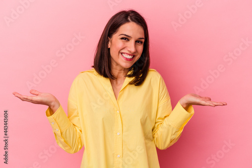 Young caucasian woman isolated on pink background makes scale with arms, feels happy and confident. © Asier