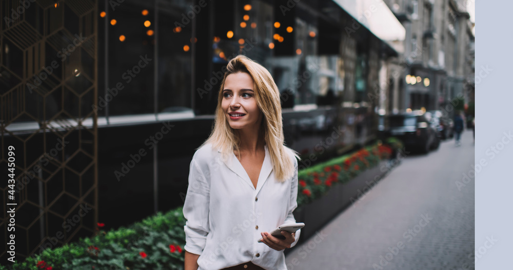 Fototapeta premium Smiling woman browsing smartphone near modern buildings on street
