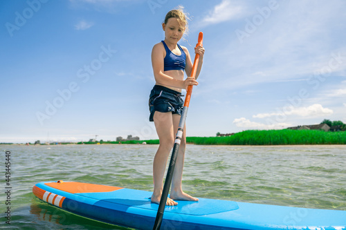 Cute little girl ecercise paddling on SUP board in sea on sunny day while summer holidays