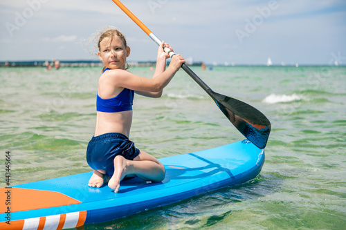 Cute little girl exercise to stay on paddle board in sea at sunny day while summer holidays © spass