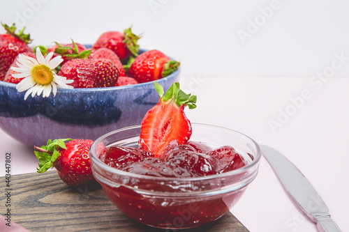 Homemade strawberry jam or strawberry jelly with fresh ripe strawberries on a white plate. Breakfast with bread toast with strawberry jam. Knife for spreading jam. Summer preserves.
