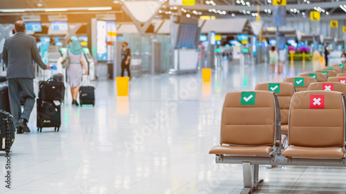 Rows empty brown chairs with the sticker sign sitting position for social distancing in waiting terminal of the airport to prevent of Corona virus (Covid-19). Safe travel new normal social distancing.