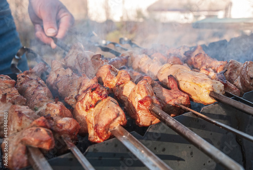 A man prepares barbecue on skewers in the grill with smoke.