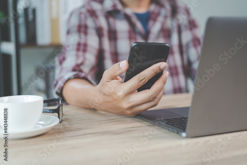 Close-up businessman holding a pen, smartphone and pointing at financial graph checking business report on wooden desk with computer laptop besided at home. Stock photo