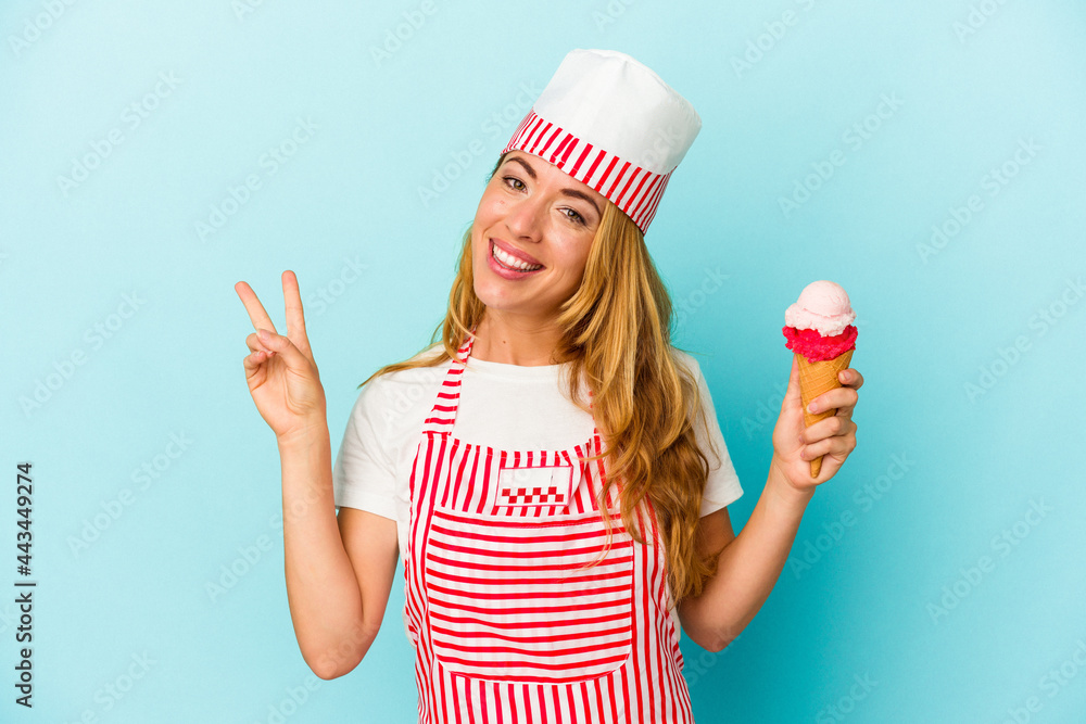Caucasian ice cream maker woman holding an ice cream isolated on blue background joyful and carefree showing a peace symbol with fingers. Caucasian ice cream maker woman holding an ice cream isolated on blue background joyful and carefree showing a peace symbol with fingers.