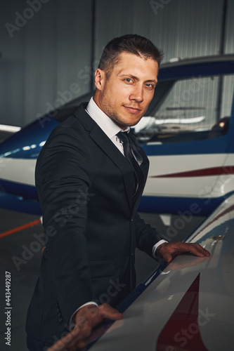 Handsome young man standing by airplane in airport hangar