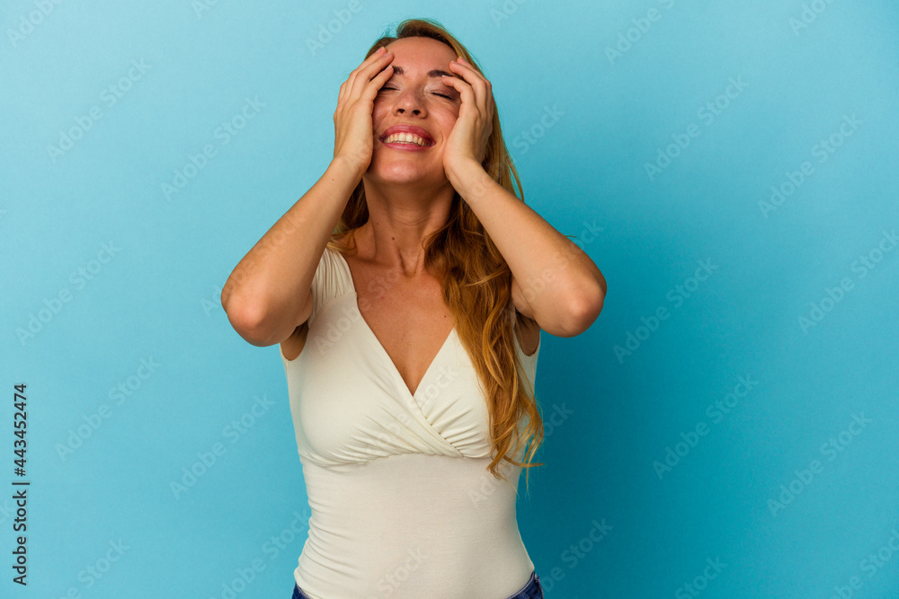 Caucasian woman isolated on blue background laughs joyfully keeping hands on head. Happiness concept. Caucasian woman isolated on blue background laughs joyfully keeping hands on head. Happiness concept.