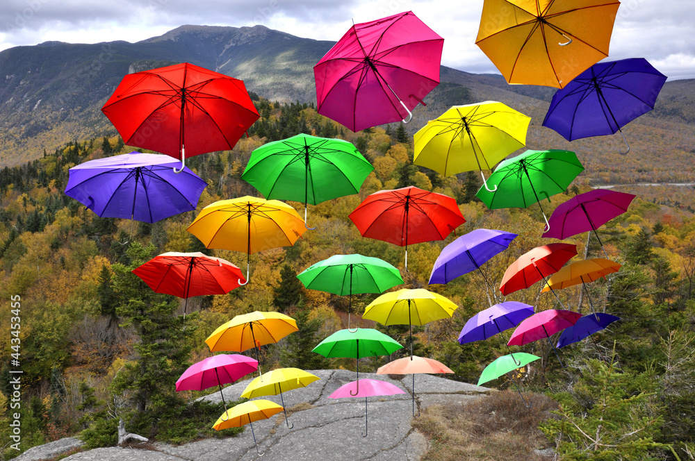 Obraz premium Unexpected and whimsical autumn scene featuring airborne parasols. Attention-grabbing image of colorful umbrellas soaring skyward over scenic Franconia Notch in White Mountains of New Hampshire.